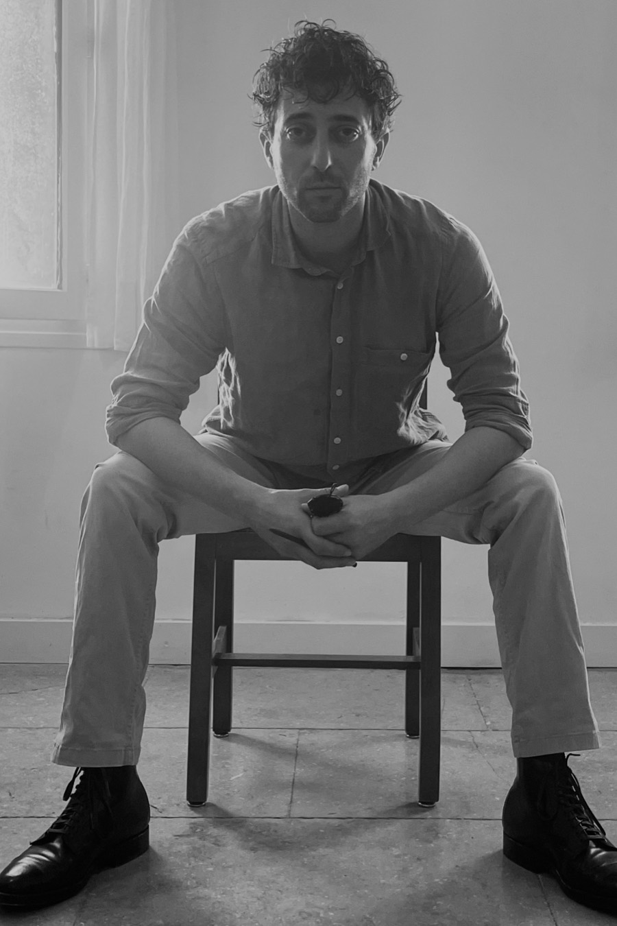 Alexandre Leloup, assis sur un tabouret bas, les mains jointes, devant un mur clair
